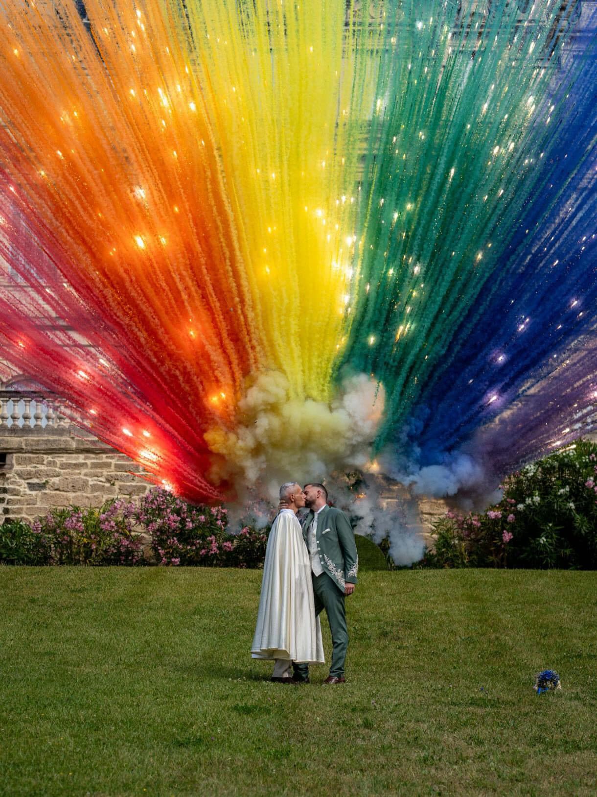 Mariés s'embrassant devant un éventail de feux arc-en-ciel dans un parc de château