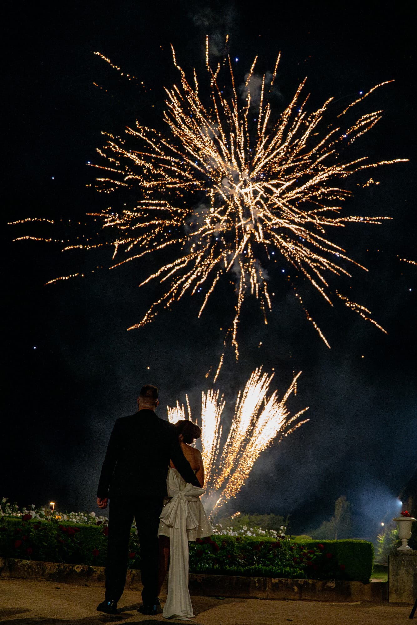 Couple de mariés admirant un feu d'artifice doré dans la nuit