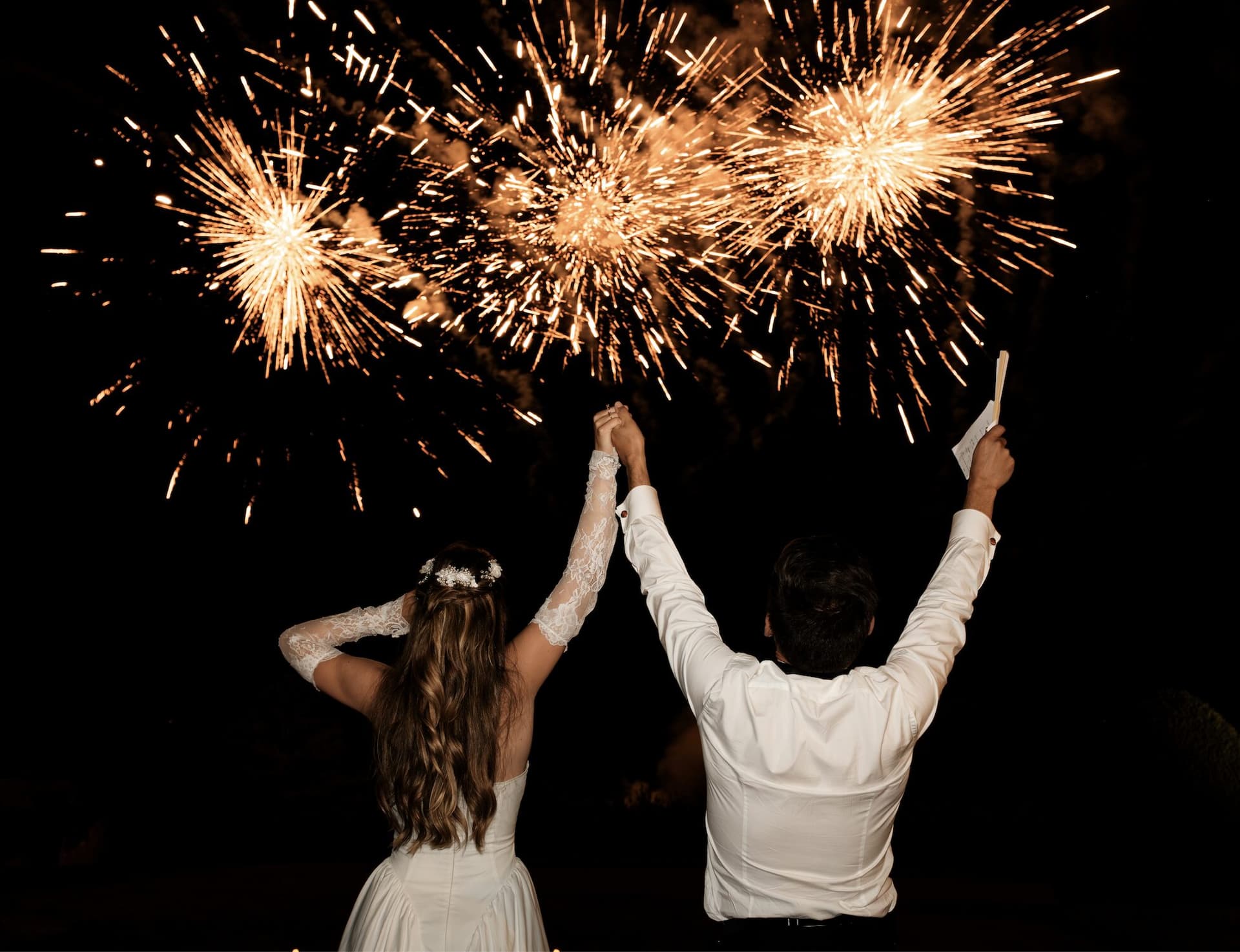 Mariés levant les bras devant un feu d'artifice doré